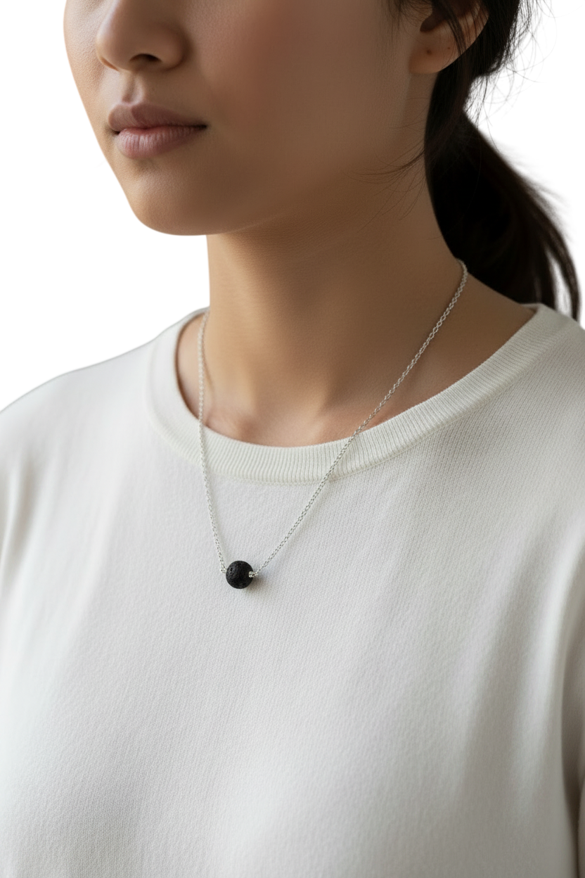 Person wearing a necklace with a black pendant on a plain background