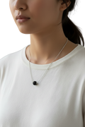 Person wearing a necklace with a black pendant on a plain background