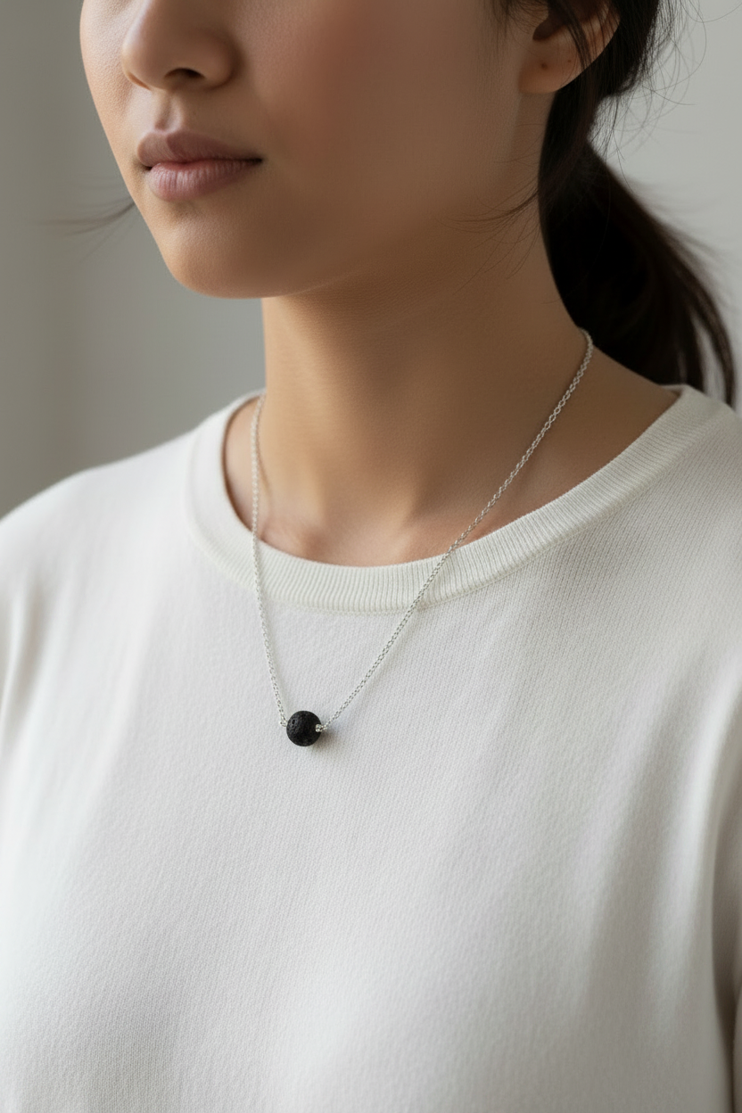 Person wearing a necklace with a black pendant on a plain background