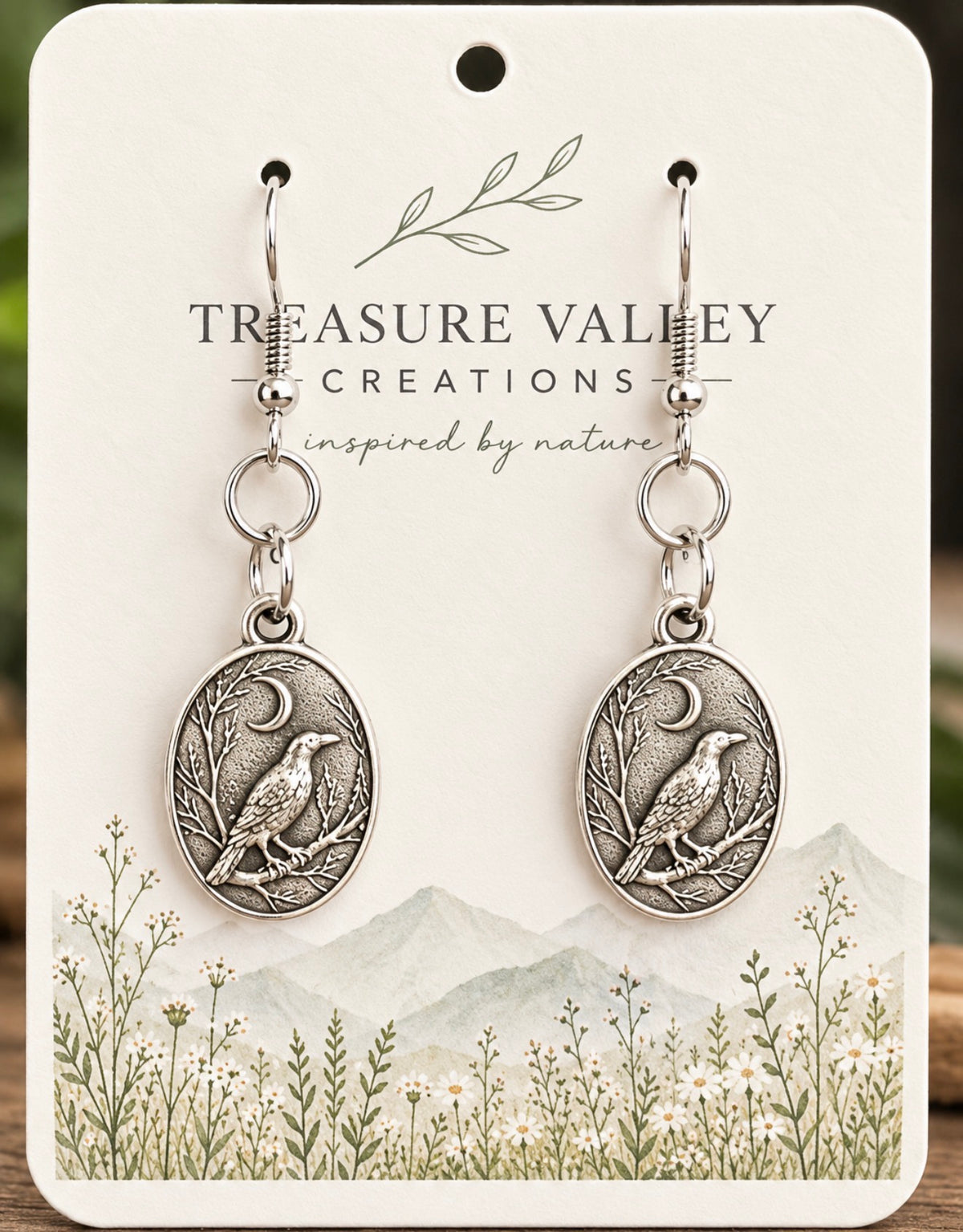 A pair of silver-toned dangle earrings with oval bird medallions and crescent moon details