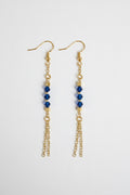 A pair of gold dangle earrings with three faceted dark blue beads on each earring, hanging from gold fishhook wires and short chain drops, shown against a plain light gray background.