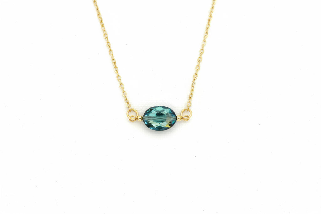 A delicate gold chain necklace featuring an oval-cut teal gemstone pendant with small gold loops on either side, shown against a plain white background.