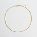 A delicate gold chain necklace with a small bead-like link pattern, a lobster clasp, and an extender chain, laid flat on a neutral light gray background.
