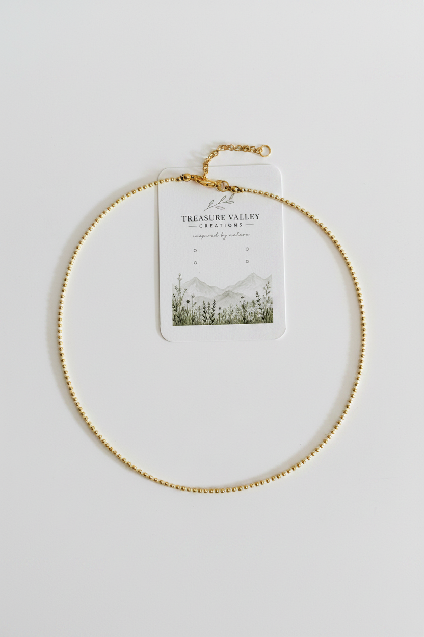 A delicate gold beaded chain necklace with an extender clasp, displayed on a white card from Treasure Valley Creations, set against a clean white background.