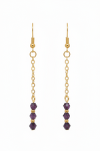 A pair of gold dangle earrings with three faceted purple beads at the bottom, shown against a plain white background.