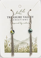 Treasure Valley Creations dangle earrings with faceted green iridescent beads and silver chain drops, displayed on a white branded card with a floral mountain illustration.