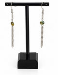 A pair of silver-toned dangle earrings with faceted olive-green beads and chain drops, displayed on a black jewelry stand against a white background.