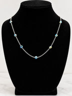 A silver chain necklace with small blue and white evil eye beads, displayed on a black velvet jewelry bust against a white background.