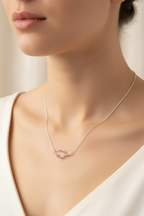 A close-up lifestyle shot of a model wearing a delicate silver chain necklace with a small, polished pink gemstone pendant.