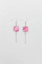 A pair of silver-toned dangle earrings with small square pink stones and short chain drops, shown on a plain light gray background.