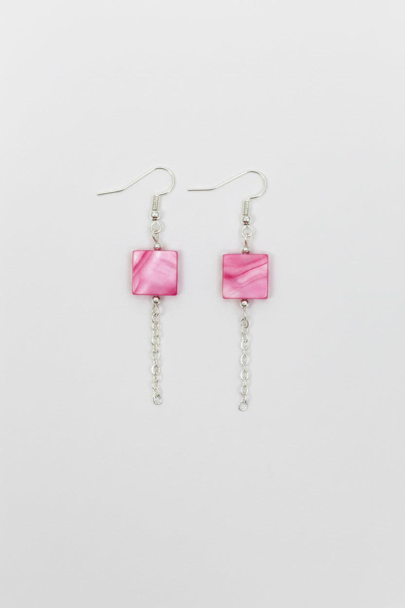 A pair of silver-toned dangle earrings with small square pink stones and short chain drops, shown on a plain light gray background.
