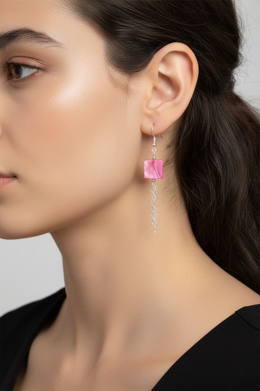 A close-up side profile of a woman wearing a dangling earring with a pink square stone and a silver chain.