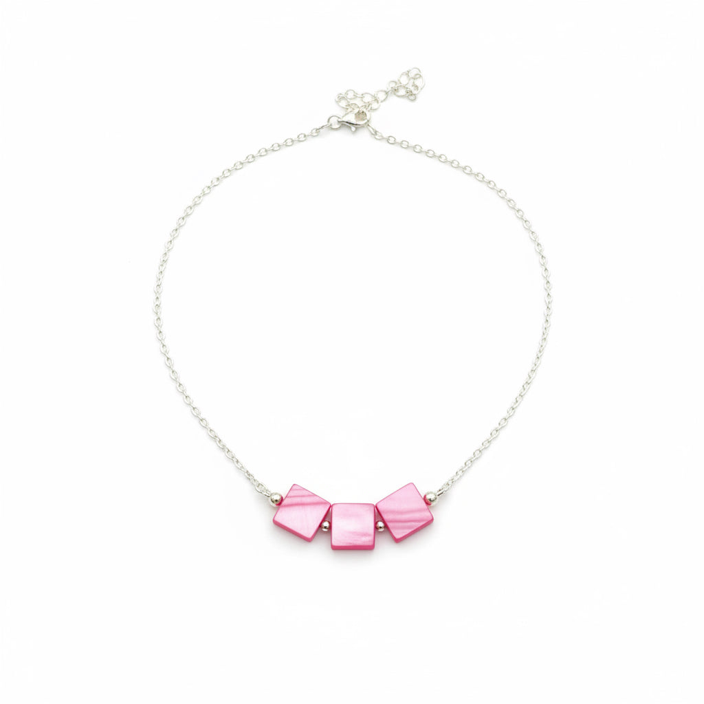 A silver chain necklace featuring three small, square-shaped pink mother-of-pearl beads on a black textured background.