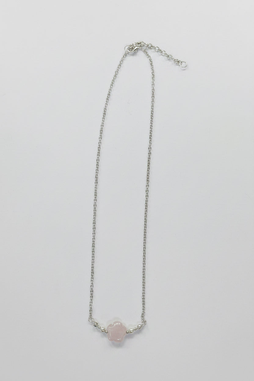 A delicate silver chain necklace featuring a small, pale pink rose quartz crystal pendant, displayed against a neutral light gray background.