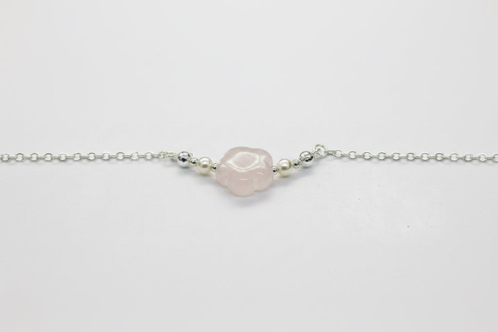 A delicate silver chain bracelet featuring a central, irregularly shaped pale pink stone bead, flanked by small metallic spacer beads, shown on a plain light gray background.