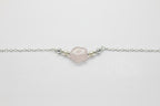 A delicate silver chain bracelet featuring a central, irregularly shaped pale pink stone bead, flanked by small metallic spacer beads, shown on a plain light gray background.