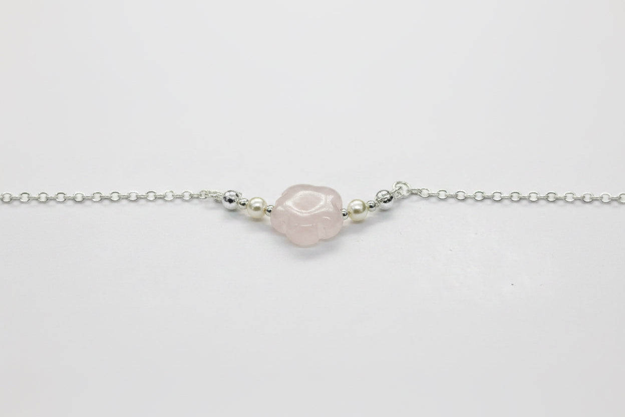 A delicate silver chain bracelet featuring a central, irregularly shaped pale pink stone bead, flanked by small metallic spacer beads, shown on a plain light gray background.