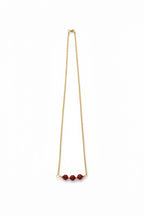 Gold necklace with red beads on a white background