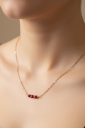 Gold necklace with red beads on a person's neck against a neutral background
