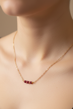 Gold necklace with red beads on a person's neck against a neutral background