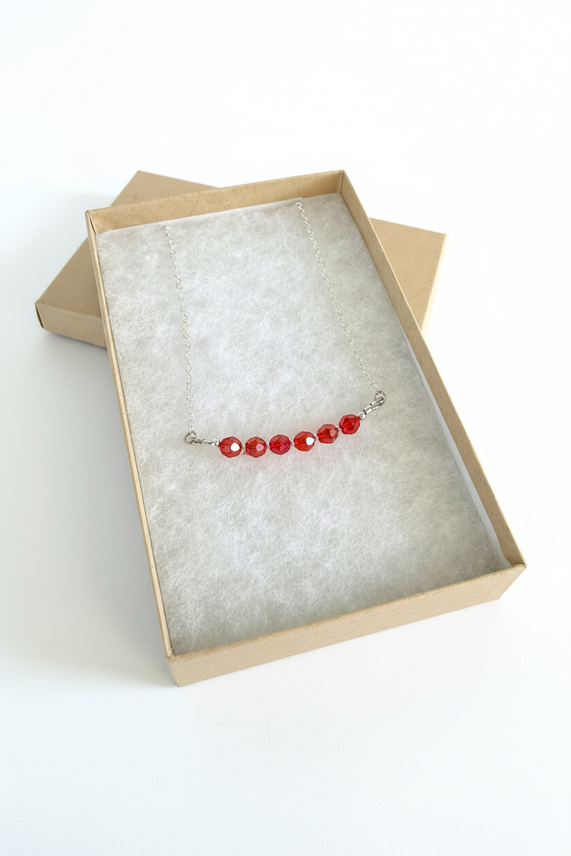 Necklace with red beads on a textured card inside an open box