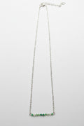 A delicate silver chain necklace featuring a short horizontal bar at the bottom adorned with small green and clear faceted beads, shown against a plain light gray background.