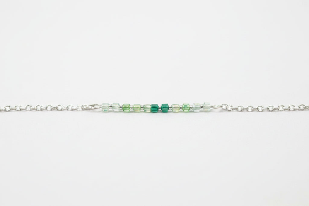 A delicate silver chain featuring a central cluster of faceted beads in light green, medium green, and emerald green, displayed on a clean white background.
