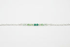 A delicate silver chain featuring a central cluster of faceted beads in light green, medium green, and emerald green, displayed on a clean white background.