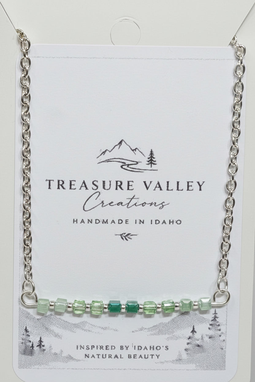 Treasure Valley Creations handmade silver chain necklace with a bar of green faceted beads, displayed on its white backing card.