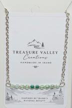 Treasure Valley Creations handmade silver chain necklace with a bar of green faceted beads, displayed on its white backing card.