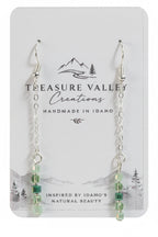 Treasure Valley Creations handmade dangle earrings with silver chains, clear faceted beads, and light green beads, displayed on a white card backing with the brand logo.