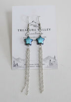 A pair of silver-toned dangle earrings with small green bead accents, displayed on a white branded card against a light gray background.