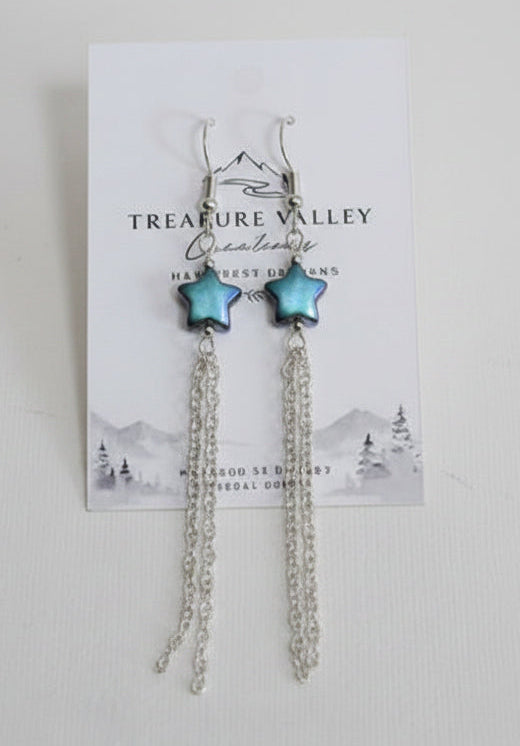 A pair of silver-toned dangle earrings with small green bead accents, displayed on a white branded card against a light gray background.