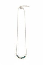 A delicate silver chain necklace featuring a curved row of faceted green gemstones at the center, displayed against a solid white background.