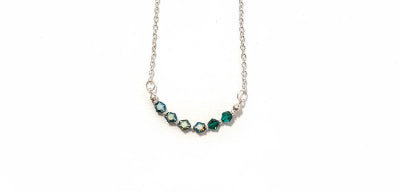 A silver-toned necklace featuring a curved bar of faceted gemstones in shades of green and dark blue, suspended on a delicate silver chain against a plain white background.