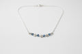 A silver chain necklace featuring a central row of small silver stars and three dark blue faceted gemstones, displayed on a textured off-white fabric background.