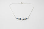 A silver chain necklace featuring a central row of small silver stars and three dark blue faceted gemstones, displayed on a textured off-white fabric background.