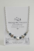 A silver-toned beaded necklace with star and faceted bead accents, displayed on a white Treasure Valley Creations card.