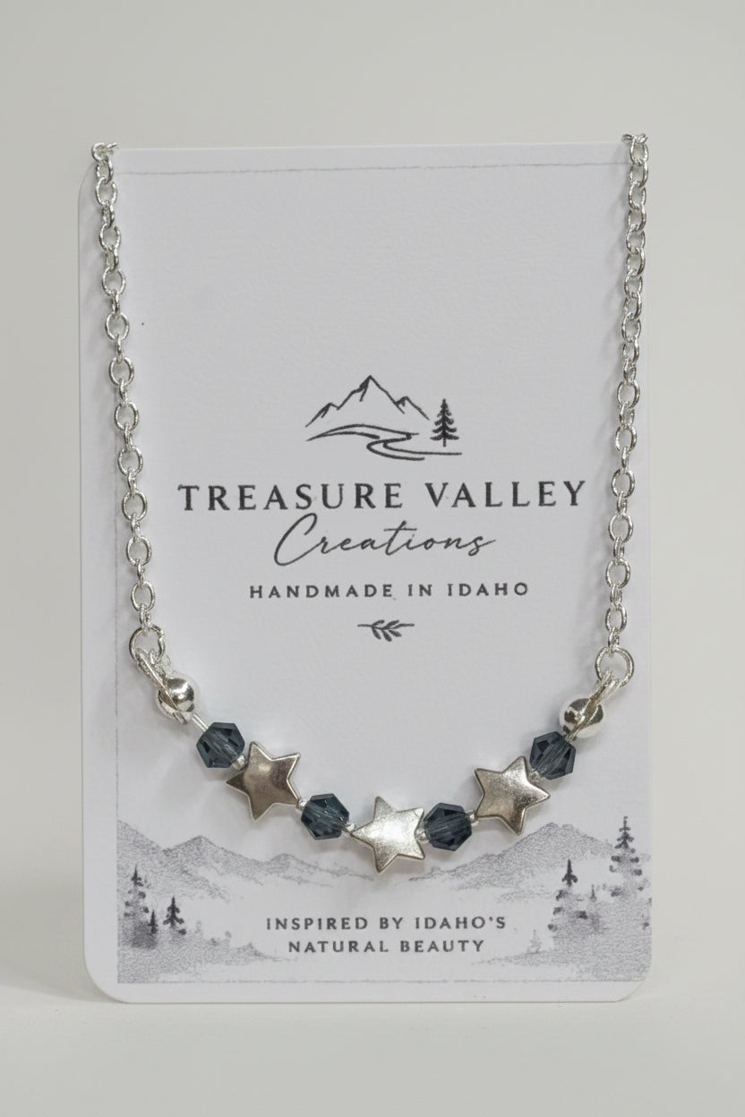 A silver-toned beaded necklace with star and faceted bead accents, displayed on a white Treasure Valley Creations card.