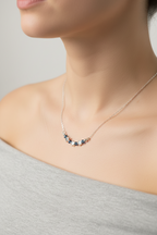 A close-up lifestyle shot of a model wearing a delicate necklace with small dark blue and rose gold beads on a fine silver chain.