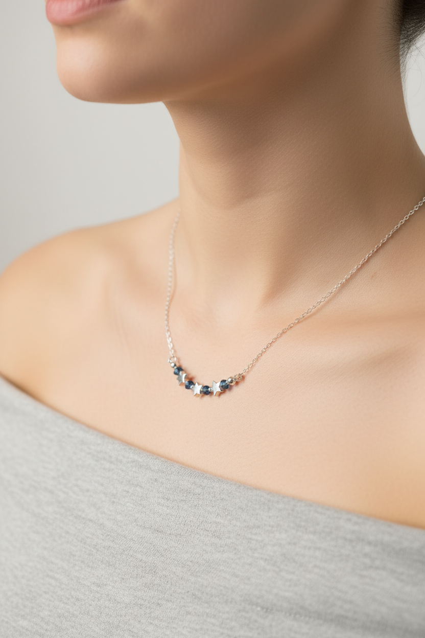 A close-up lifestyle shot of a model wearing a delicate necklace with small dark blue and rose gold beads on a fine silver chain.