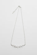 A delicate silver chain necklace featuring a curved bar of small, clear, faceted stones at the center, displayed against a plain light gray background.