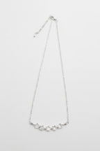 A delicate silver chain necklace featuring a curved bar of small, clear, faceted stones at the center, displayed against a plain light gray background.