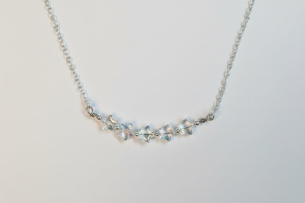 A silver-toned chain necklace featuring a central cluster of clear, faceted crystal beads on a plain light gray background.