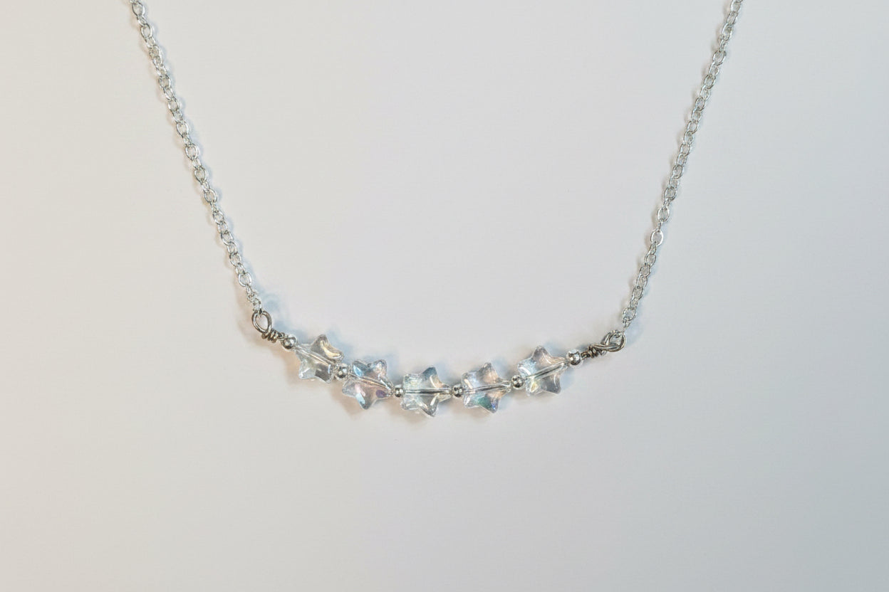 A silver-toned chain necklace featuring a central cluster of clear, faceted crystal beads on a plain light gray background.