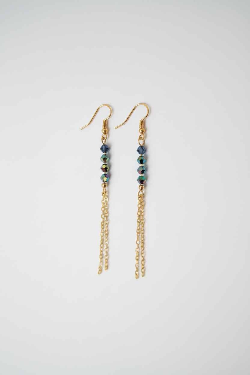 A pair of gold dangle earrings with small dark blue beads and iridescent green accents, hanging against a plain light gray background.