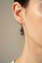 A close-up of a model's ear wearing a gold dangle earring with faceted beads and a long gold chain.