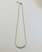 A delicate gold chain necklace with a small curved bar of light blue beads at the center, displayed against a plain white background.