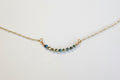 A delicate gold chain necklace featuring a short, curved bar of faceted beads in blue, green, and gold, displayed on a clean white background.