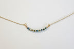 A delicate gold chain necklace featuring a short, curved bar of faceted beads in blue, green, and gold, displayed on a clean white background.